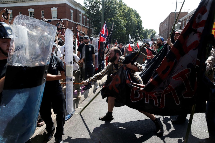 A man in a line of protesters lashes out with a stick against a line of rival activists.