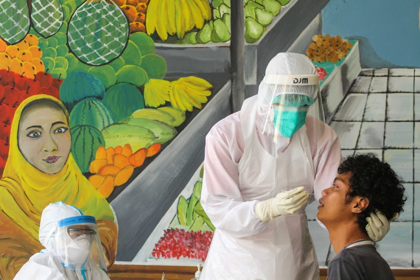 Healthcare workers take a swab sample from a vendor at a traditional market in Indonesia.