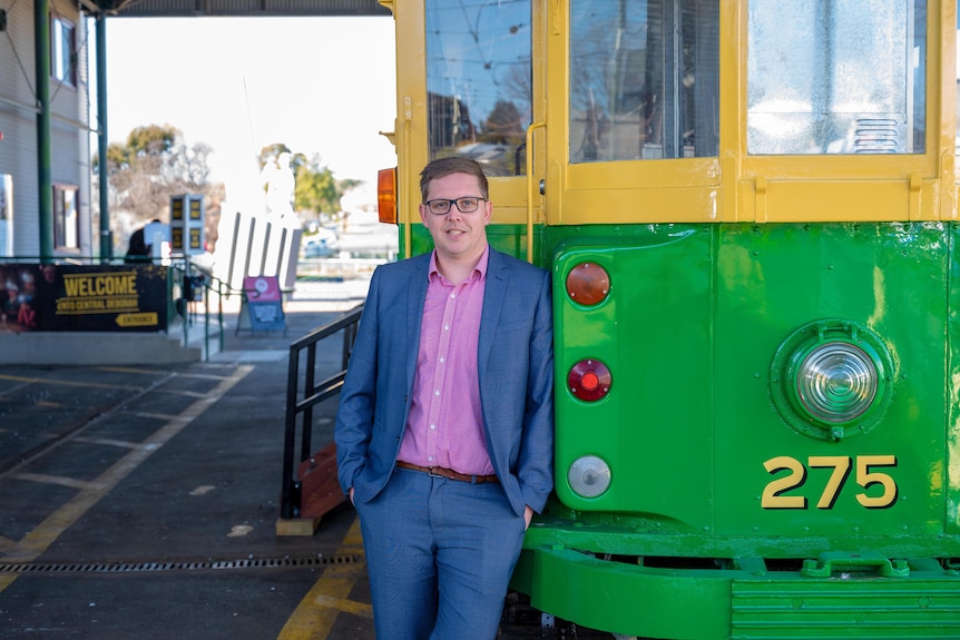 A man in a blue suit stands in front of a heritage tram.