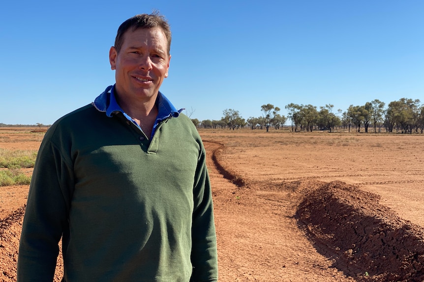 A man stands in a paddock in front of banks of compact soil, built to slow the spread of water after rain