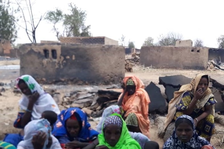 Women and children sit in the remains of a burned village.