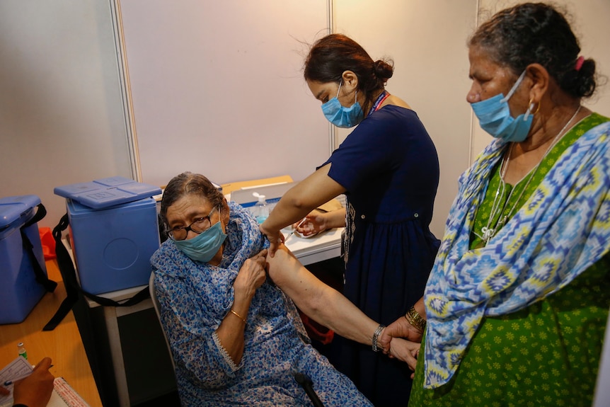 An elderly woman, left, holds the arm of her domestic helper as she receives a COVID vaccine 
