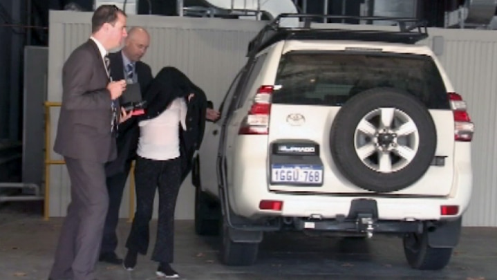 A Perth mother hides under a black jacket while being escorted by two police officers.