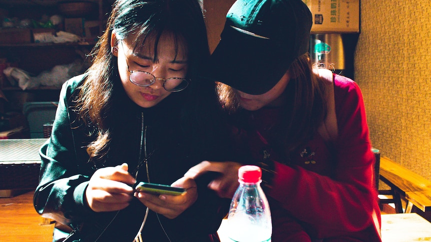 two women hunch over a phone texting