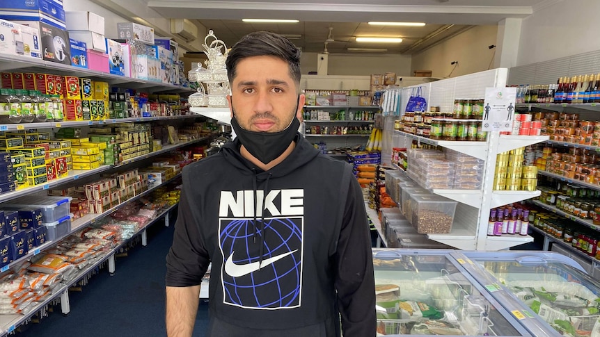 Man stands with a black face mask pulled down in a small grocery store.