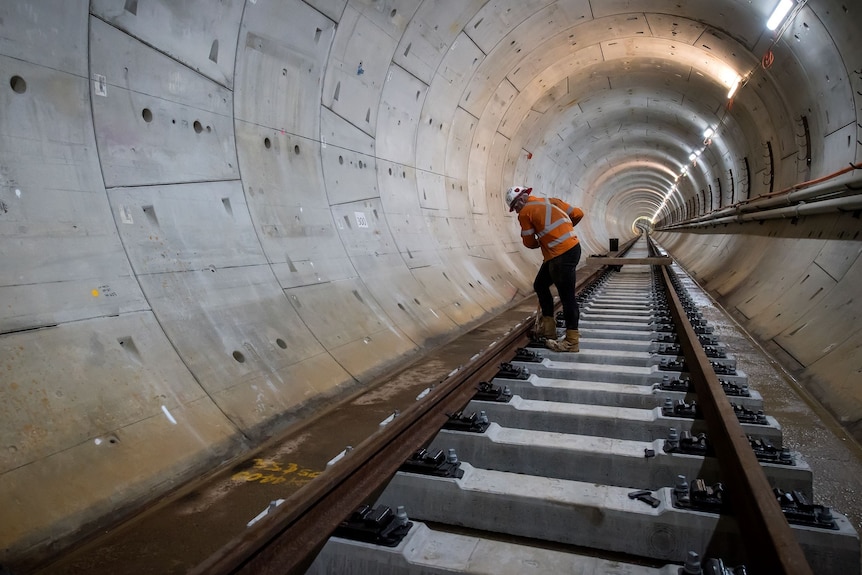 a worker wearing a hard hat fixing a rail line inside a tunnel