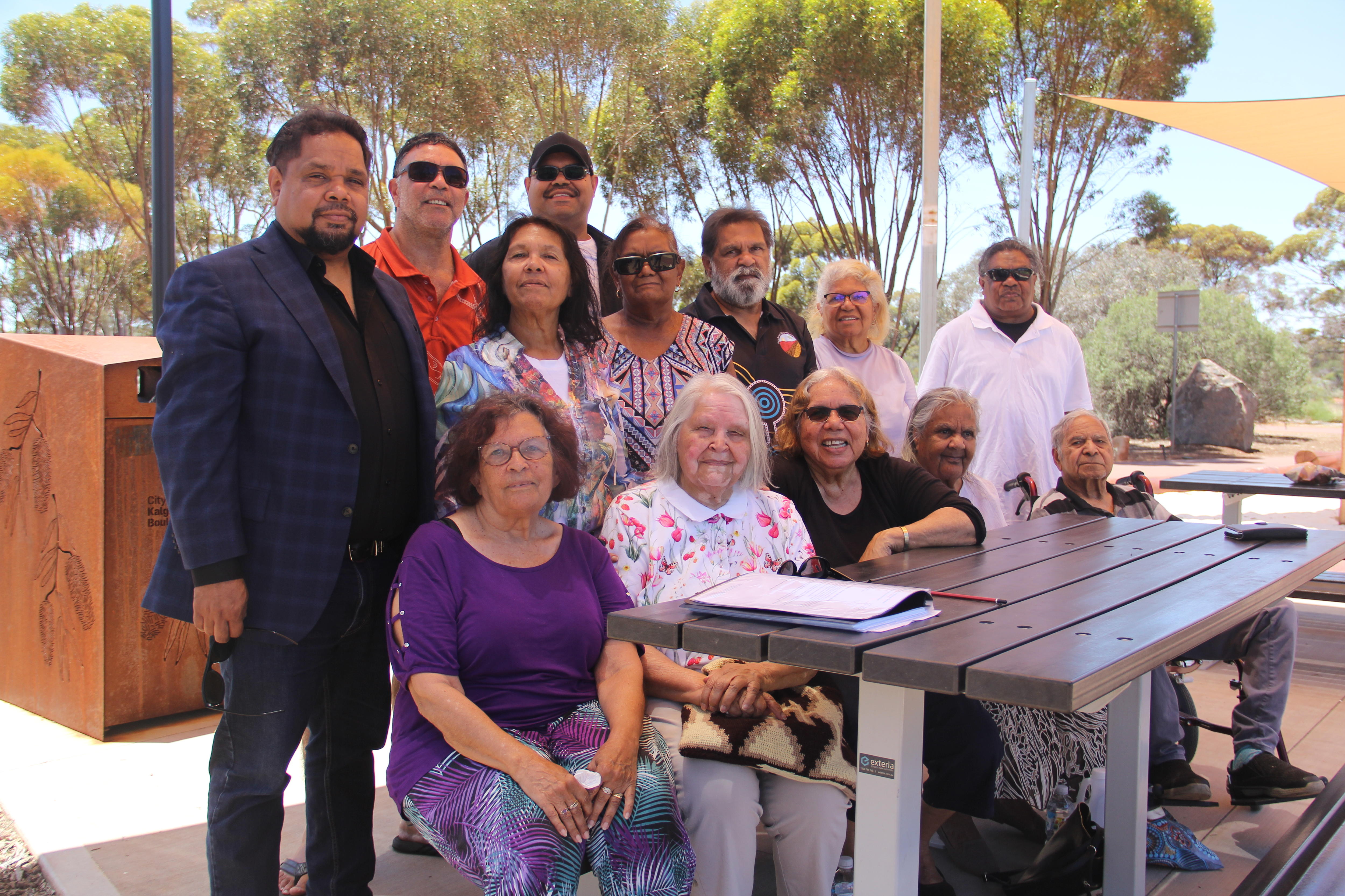 Una familia se sienta y permanece junta alrededor de un banco del parque y mira a la cámara.
