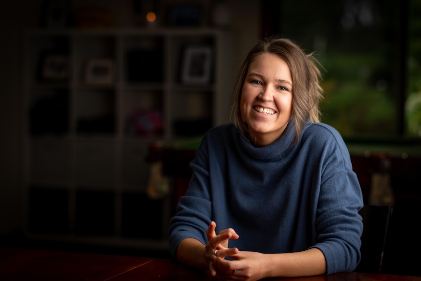 A woman in a blue jumper smiling in a dimly lit room