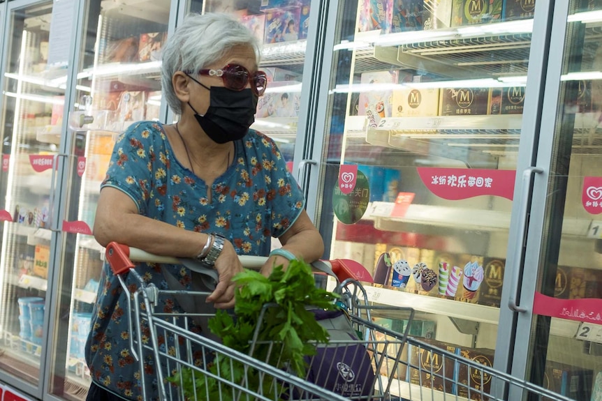 Grey-haired woman wearing black mask, looking at groceries