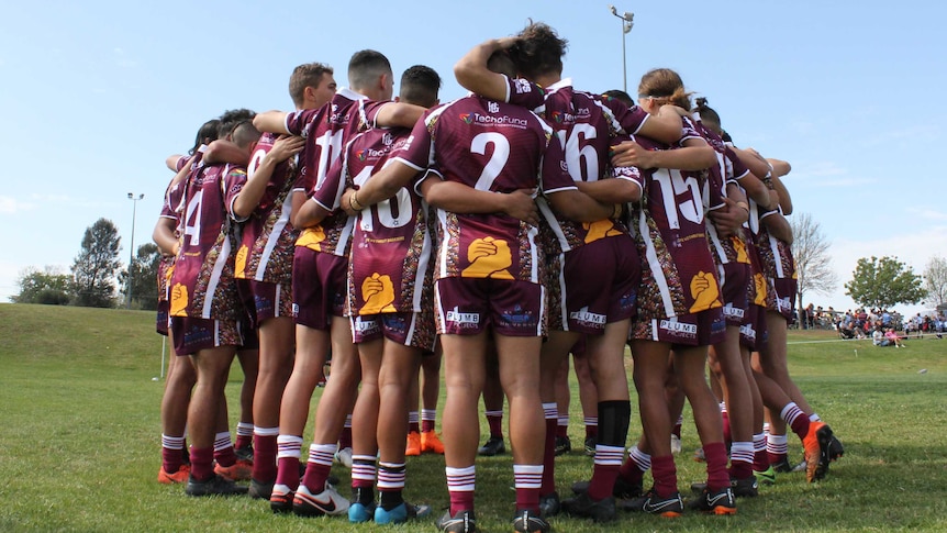 A group of young rugby players in a huddle in an open field.