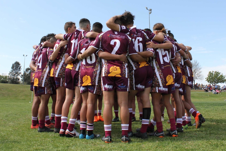 A group of young rugby players in a huddle on an open field