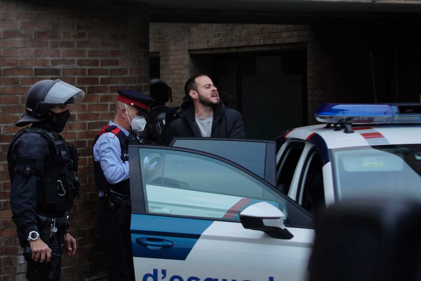 A man is put into a police car by police wearing masks.