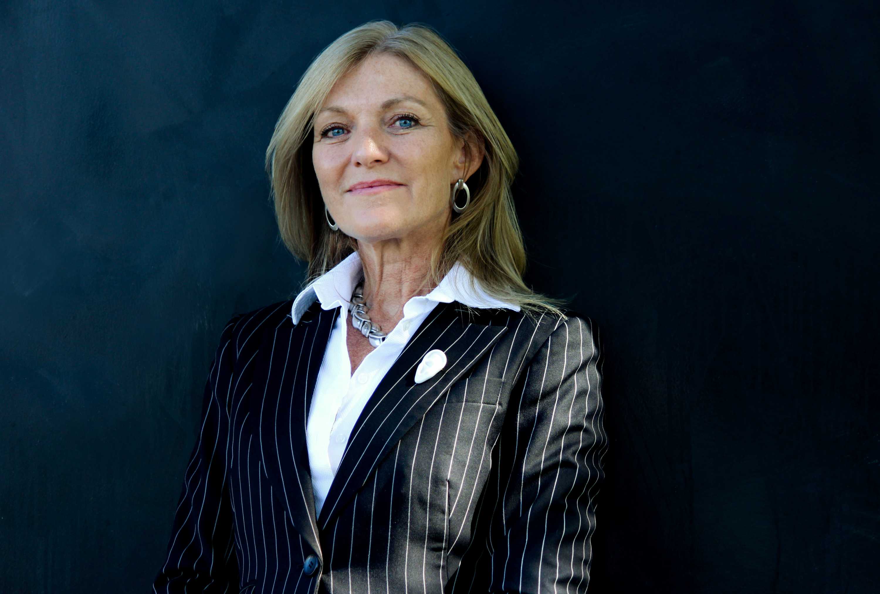 Fiona Patten wears a black pin stripe jacket over a white shirt and smiles the camera