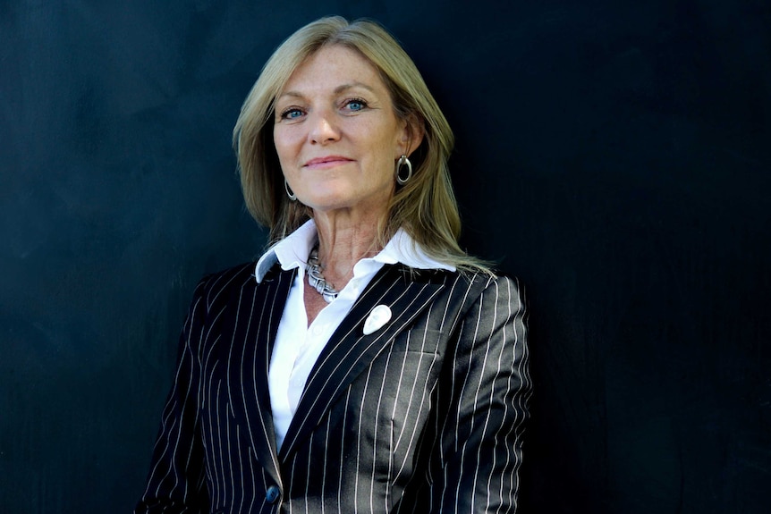 Fiona Patten wears a black striped jacket over a white shirt and smiles at the camera