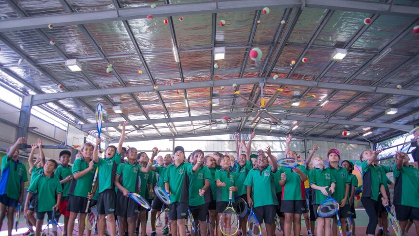 Dozens of school children throw tennis balls into the air.