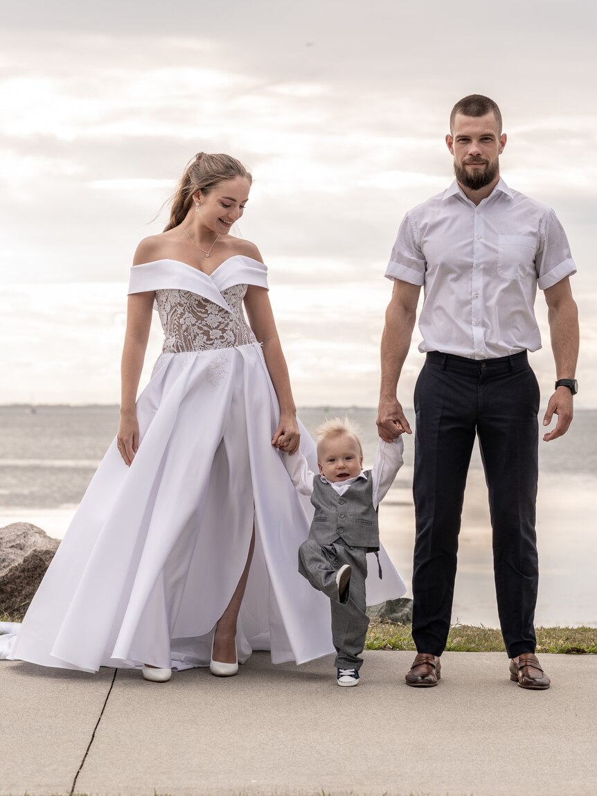 A young couple in wedding clothes holding hands with a toddler. 