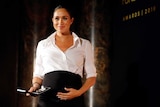 Meghan Markle smiling in a white shirt and black skirt