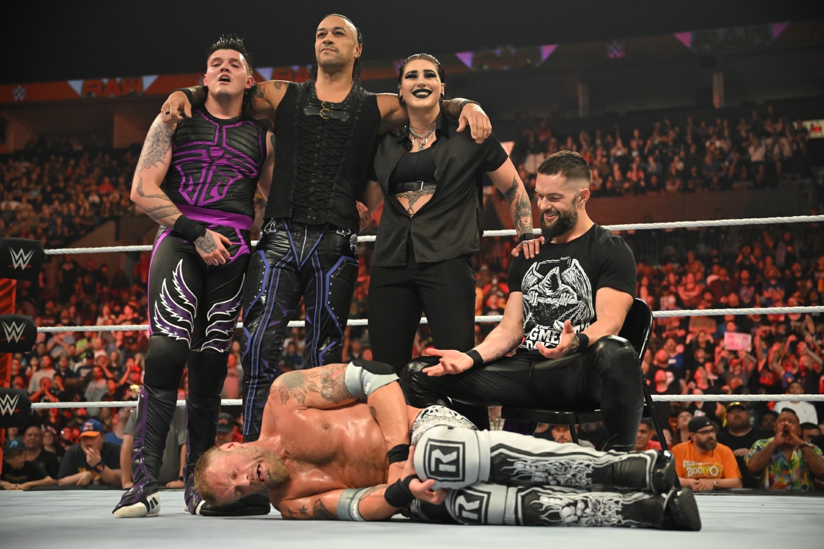 A man lays on the ring mat, while three men and a woman look proud standing over his body.