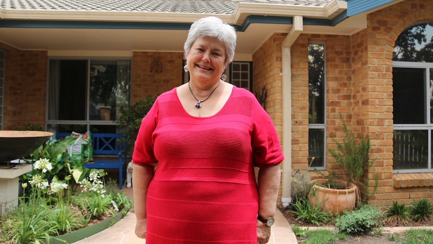 Fiona wears a pink top and stands in front of her Canberra home.