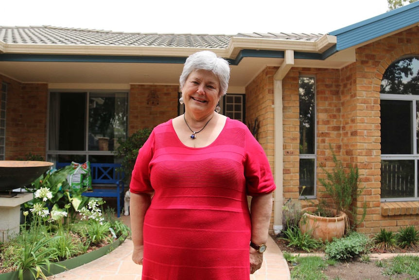Fiona wears a pink top and stands in front of her Canberra home.