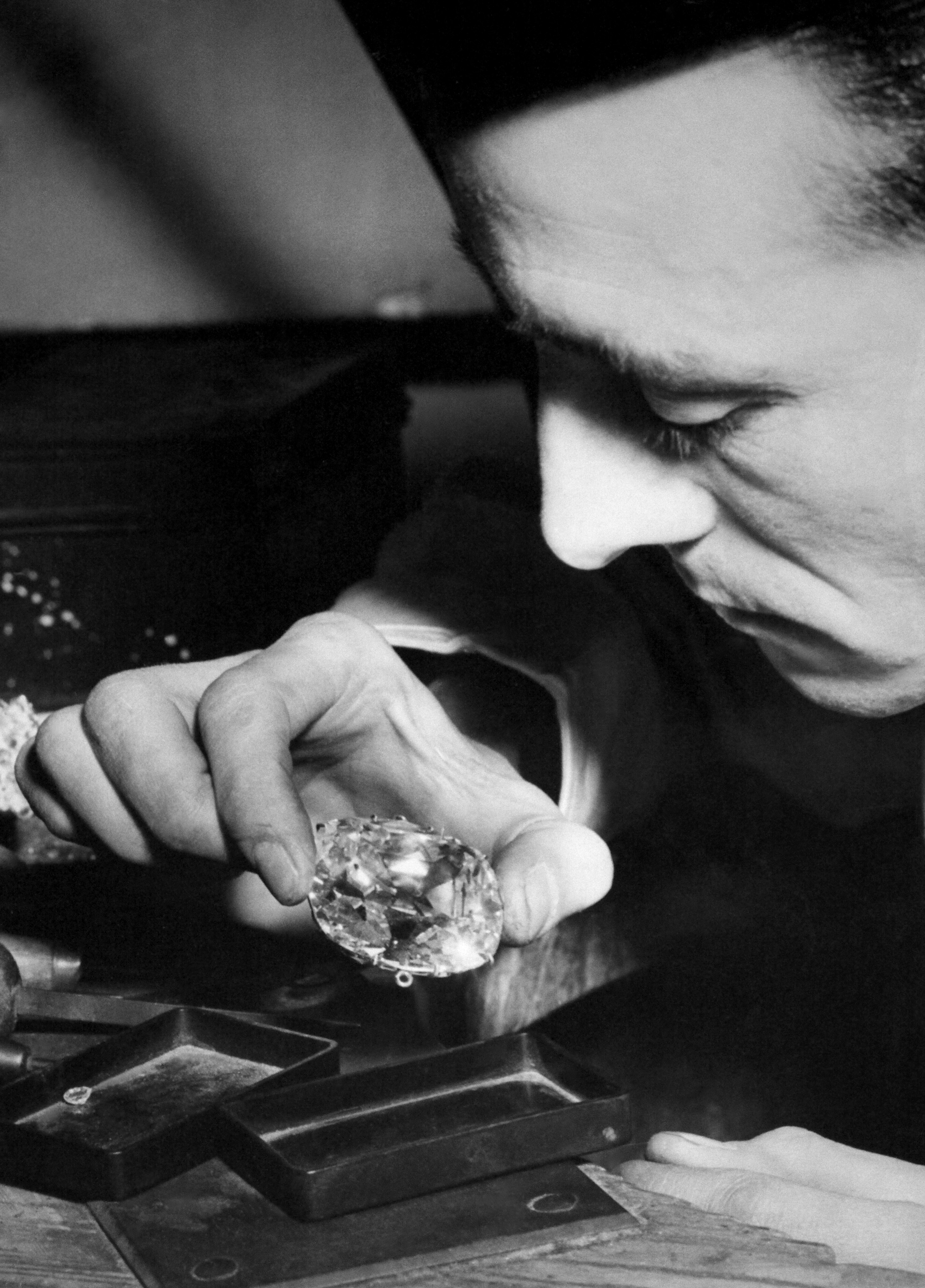 A close-up on a man's hand holding a large diamond shows him appraising the stone