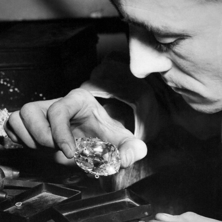 A close-up on a man's hand holding a large diamond shows him appraising the stone
