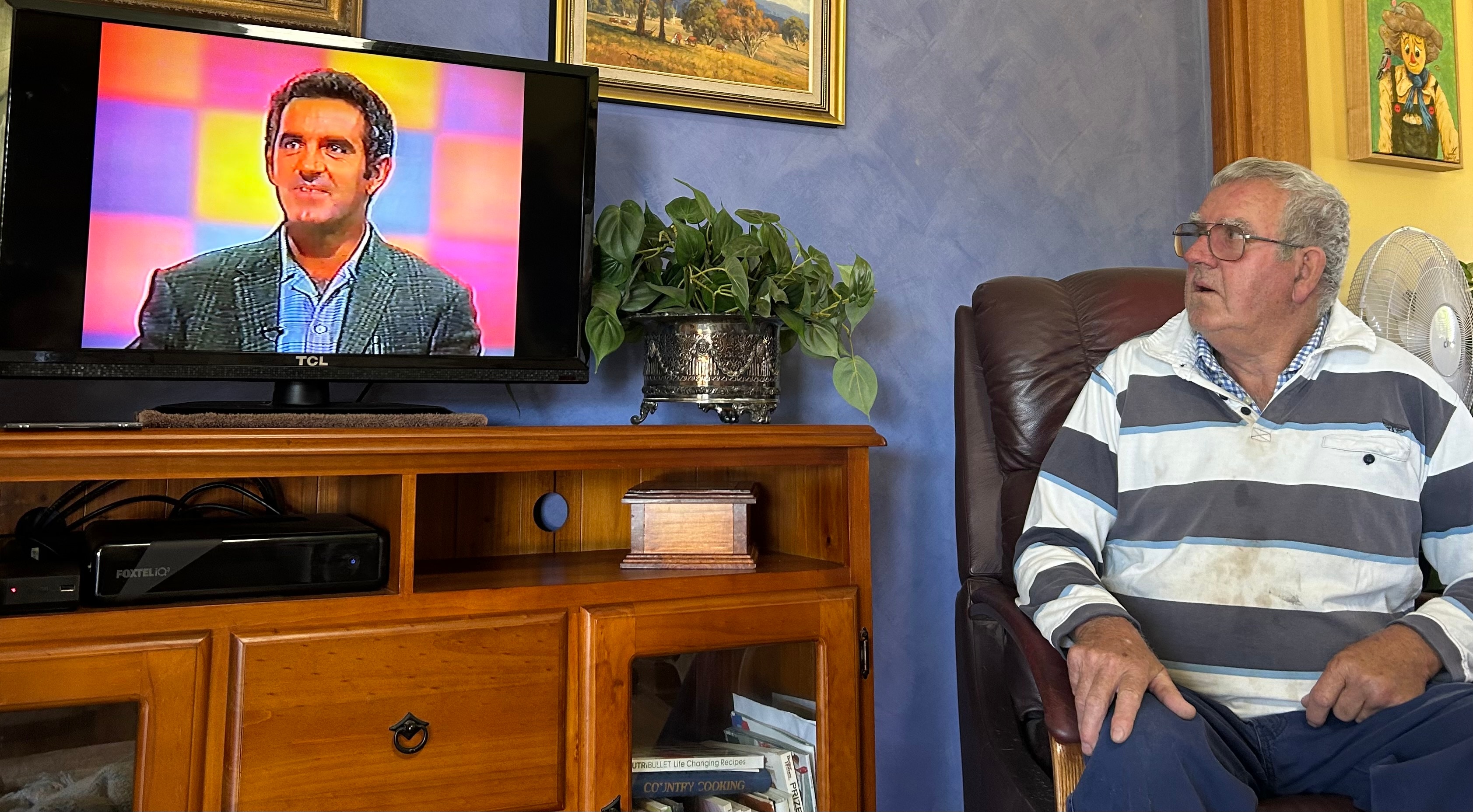 A man sitting in his lounge room watching his younger self on TV.