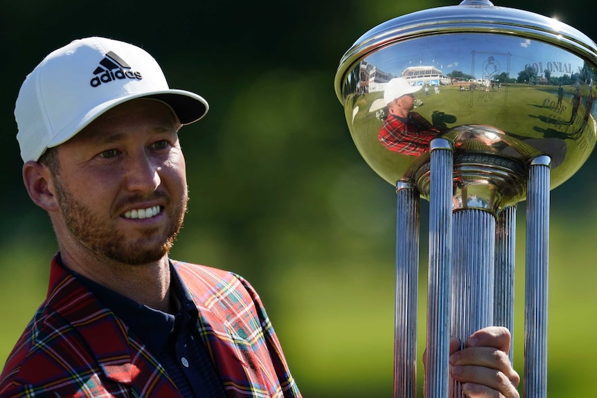 Daniel Berger holds a trophy and smiles, wearing a tartan jacket