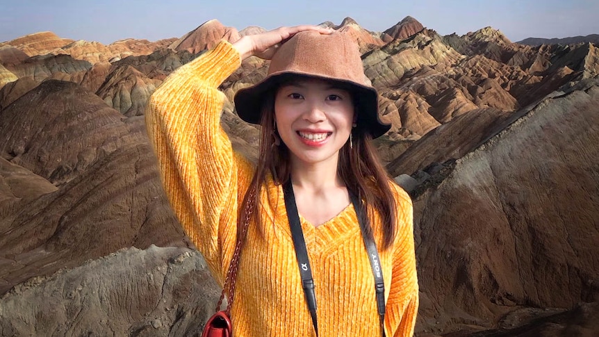 Woman wearing bright yellow jumper and hat in front of mountain range