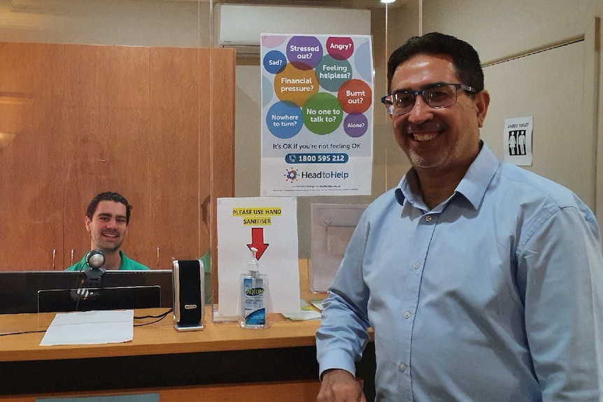Dr Ahmad stands smiling in the reception area with a male receptionist in the background.