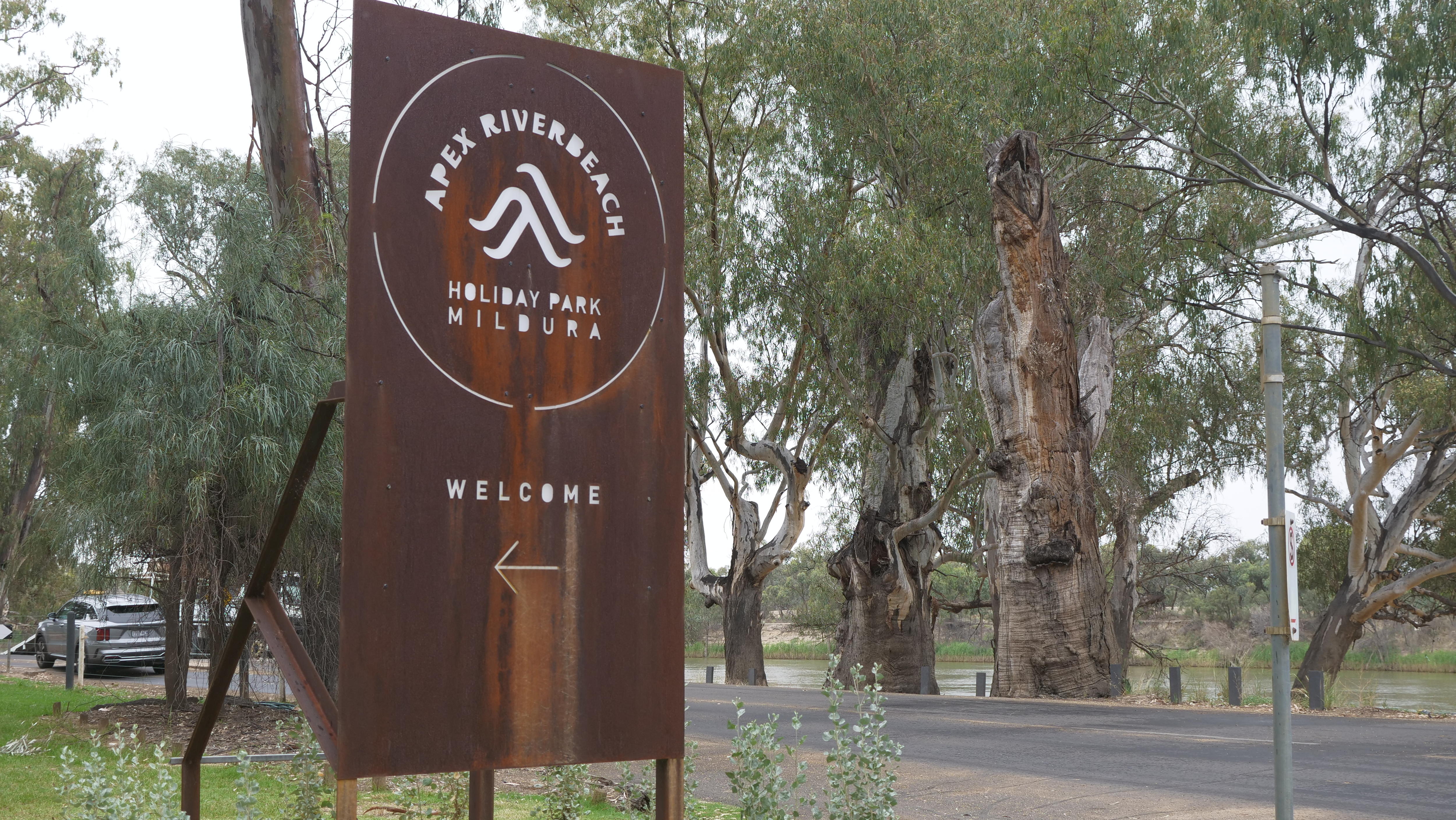 A rusted metal sign outside a caravan park that reads Apex Riverbeach