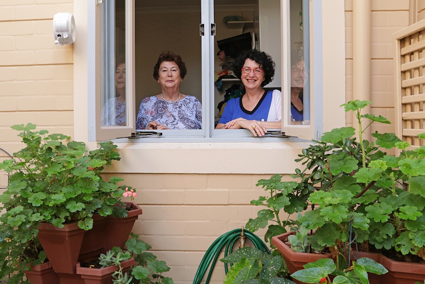 Two women overlook a garden from a window.