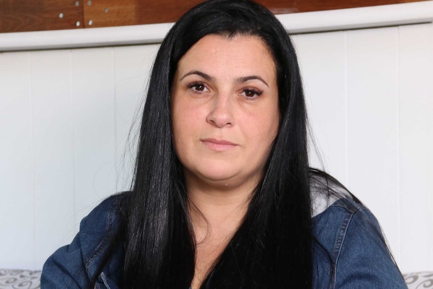 A woman with long black hair and a denim jacket sits on a couch.