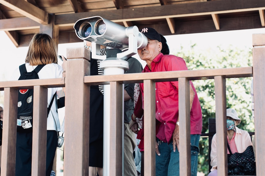 A man stands behind a lookout dressed in a pink shirt and jeans.