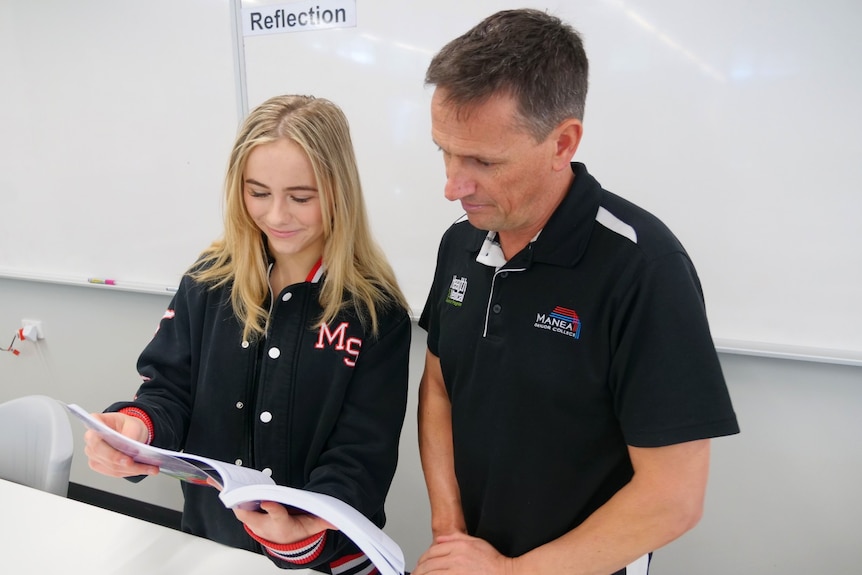 A year 12 female student looks over a human biology text book with her teacher. 