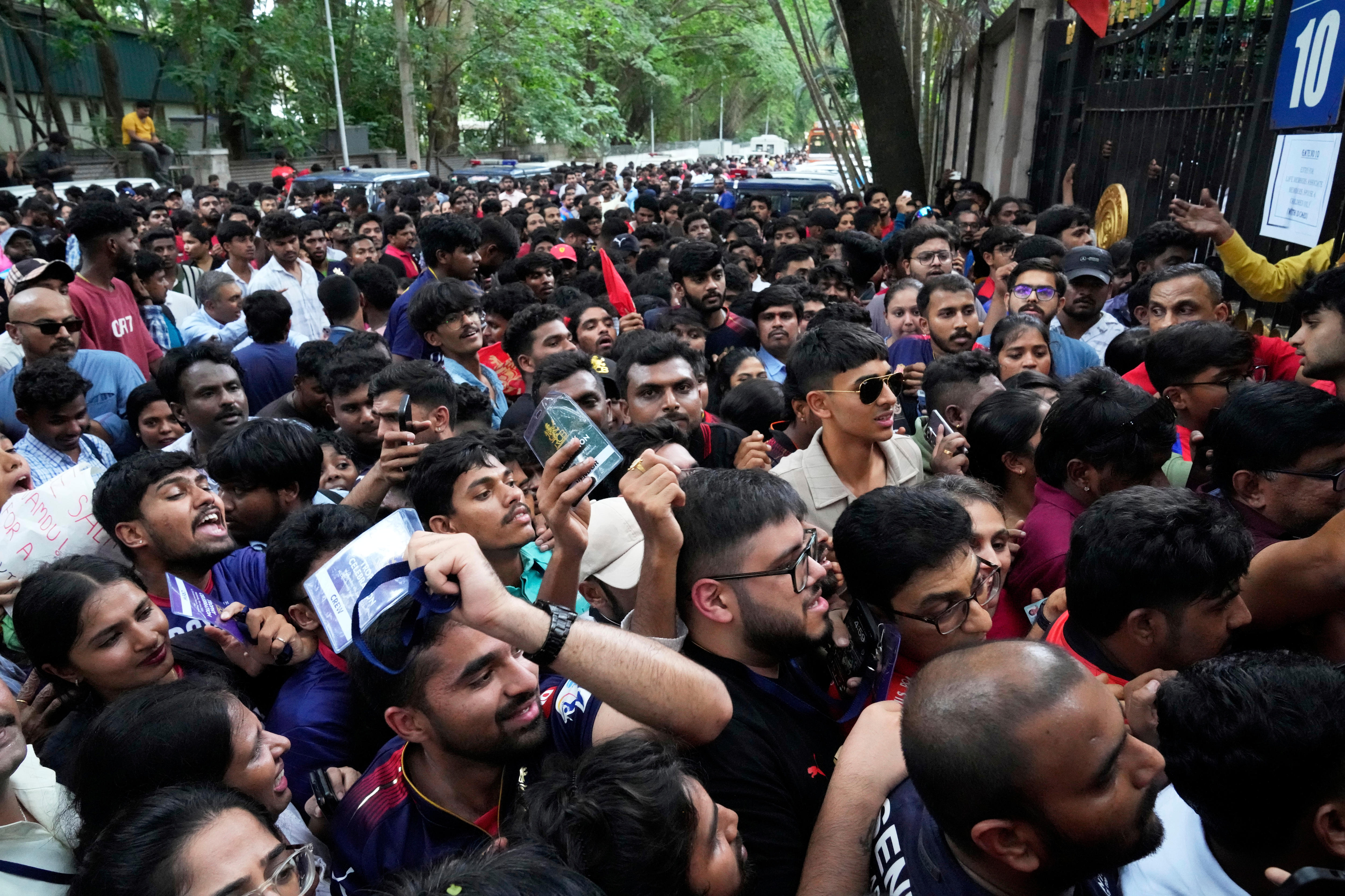 A large crowd of dark-haired men and woman packed along a fenceline on an Indian street