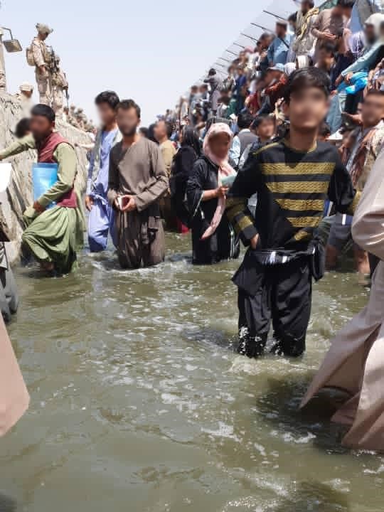 Een groep Afghaanse mensen staat in het water op de luchthaven van Kabul, hun gezichten wazig vanwege de privacy. 