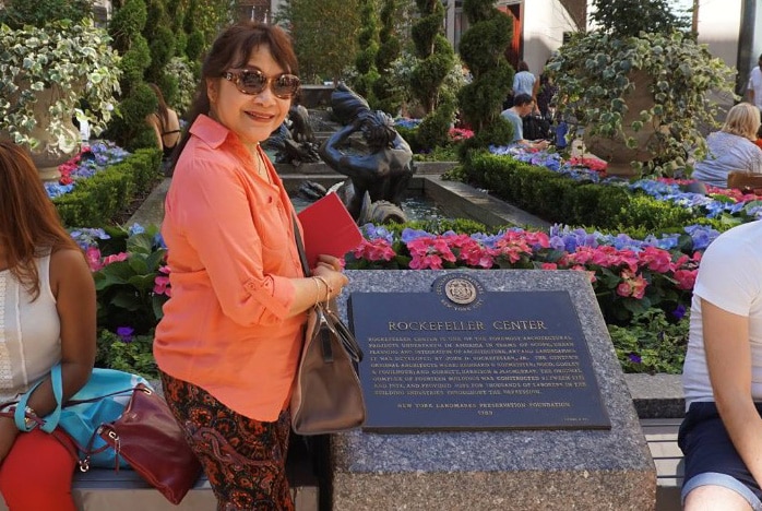 Luz Freeman with a Rockefeller Centre plaque in a New York courtyard garden.