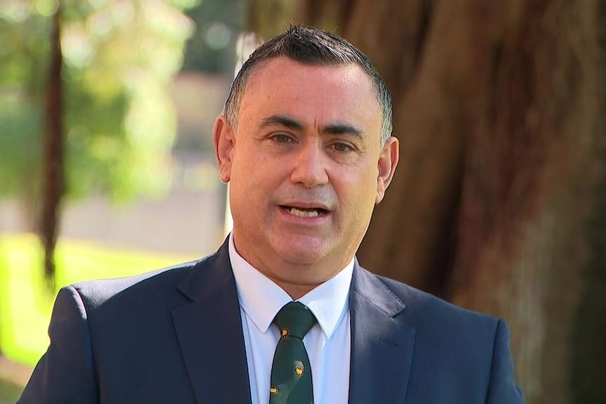 John Barilaro, middle-aged, dark-haired and attired in a dark suit, stands outside speaking the the media.