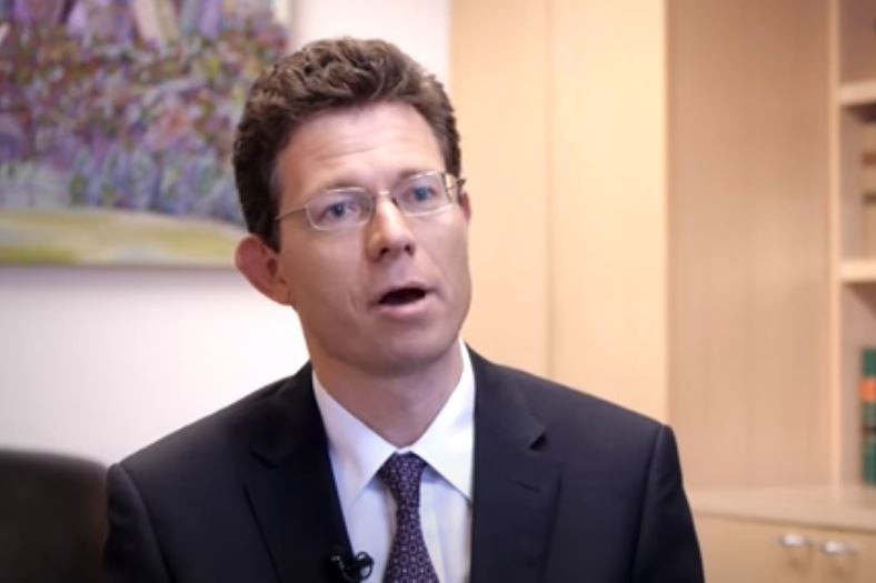 A man with brown hair and a suit, wearing glasses.