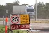 A COVID testing station sign with a truck passing in the background on the other side of the road