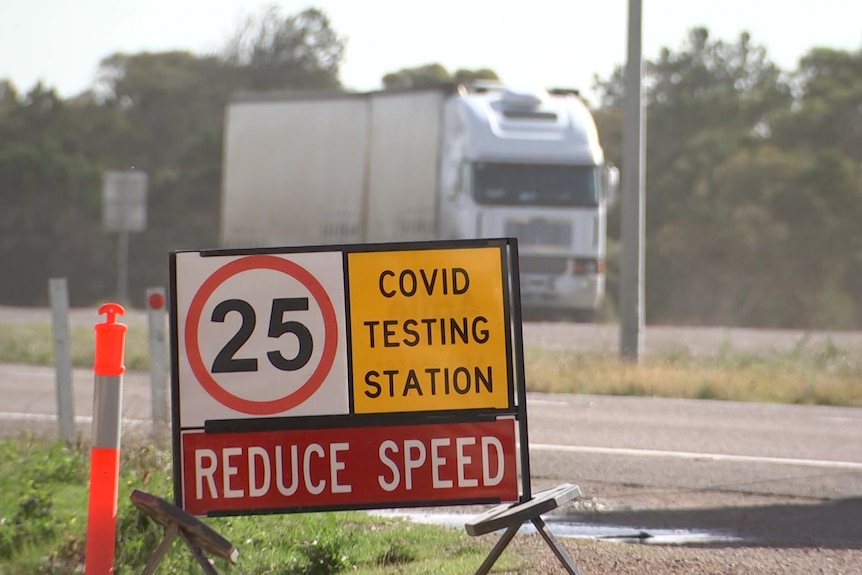 A COVID testing station sign with a truck passing in the background on the other side of the road