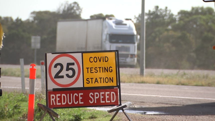 A COVID testing station sign with a truck passing in the background on the other side of the road