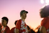 Teenager with red and white jersey stands on a football pitch against a burnt orange sky.