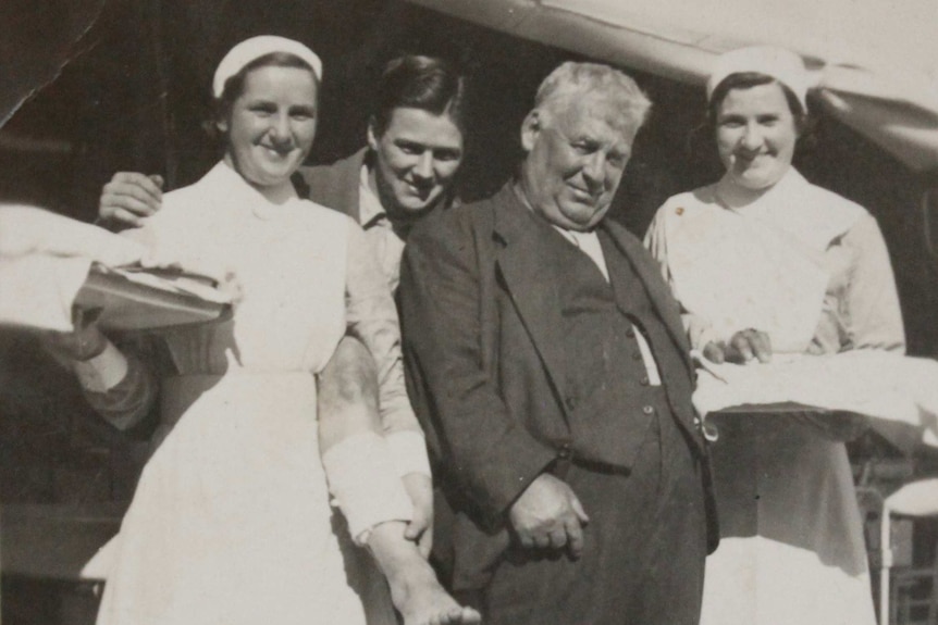 Sepia photo of two young nurses dressed in white, a young man and an older man also standing next to each other