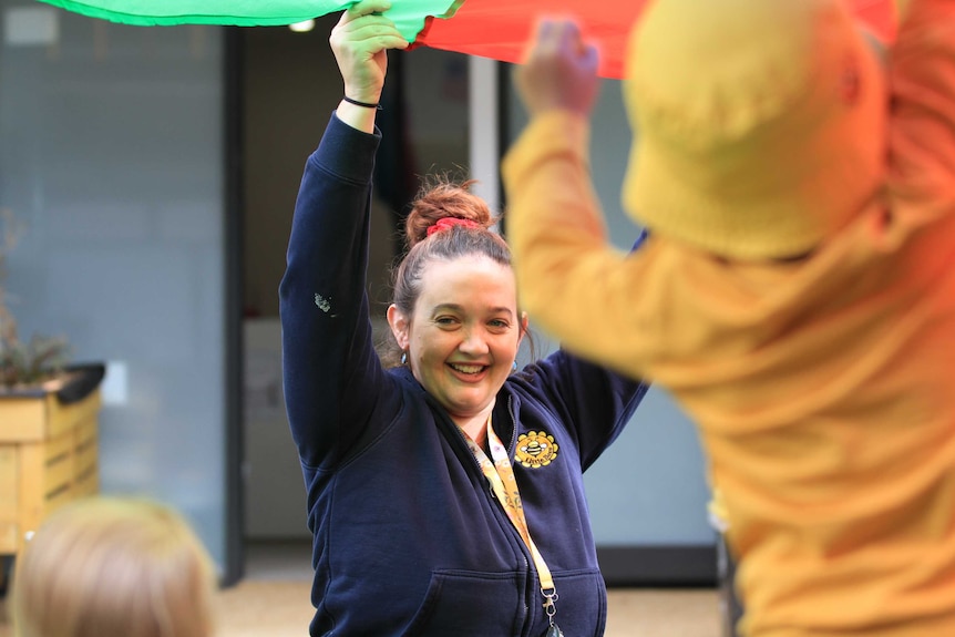 Emily Donnan in a dark blue top, smiling and waving coloured material above her head
