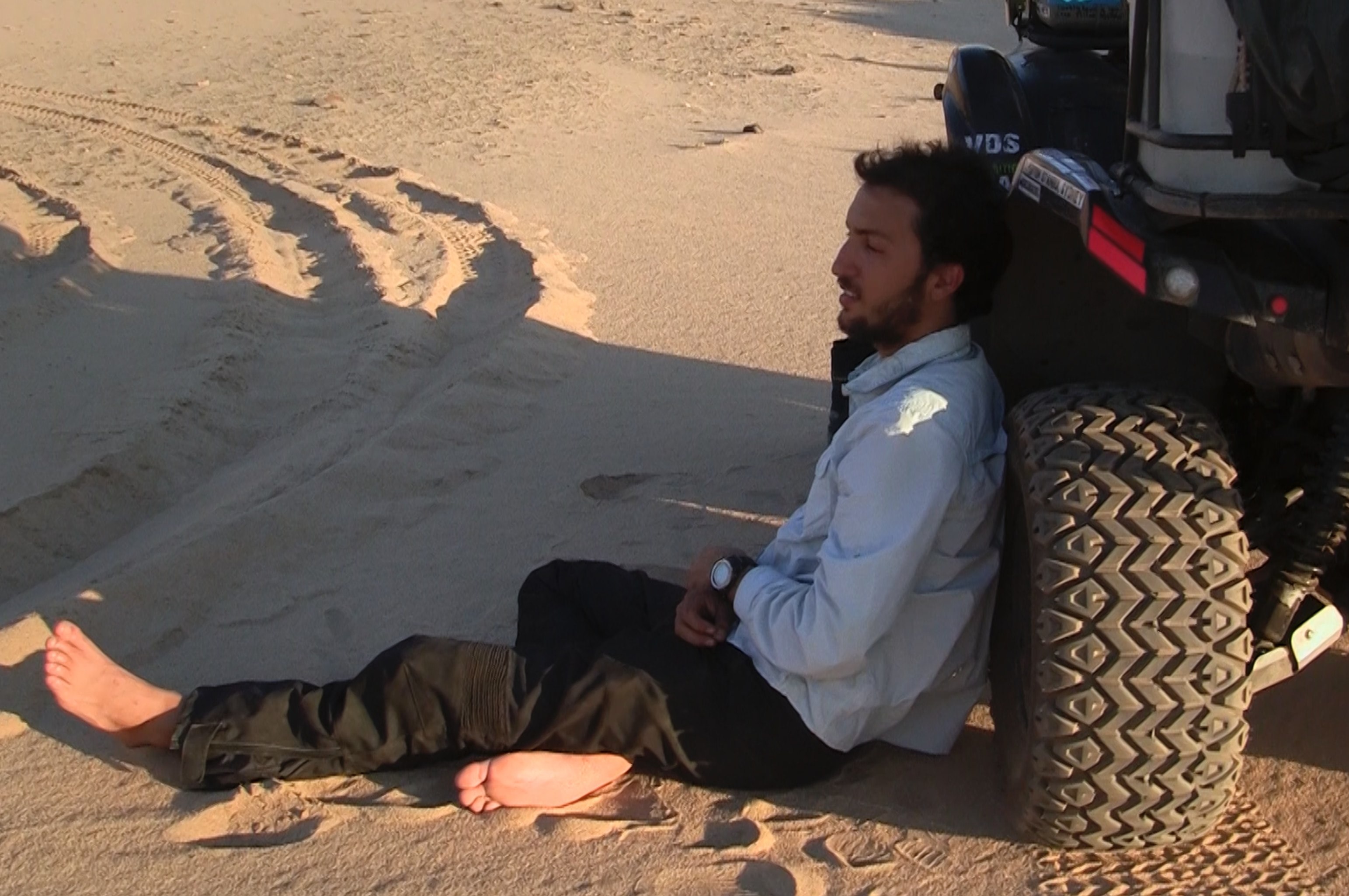 A man rests on a car tire in the desert