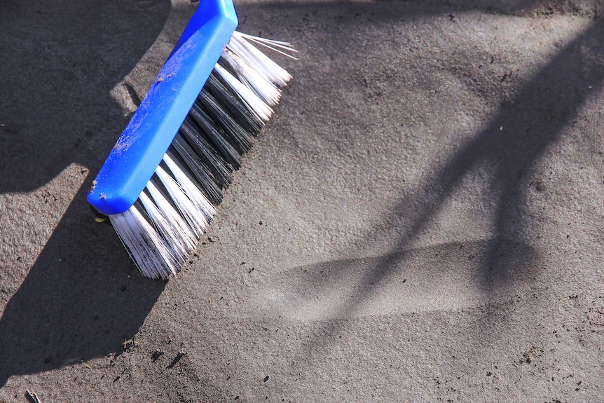 Close up of a dustpan brush on a rock surface with a rounded edge groove next to it