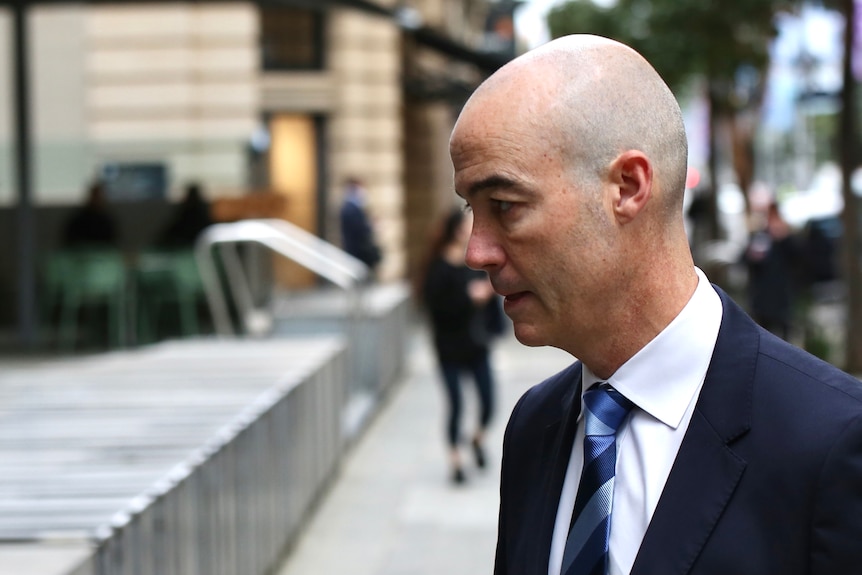 Side profile headshot of a man on a busy street.