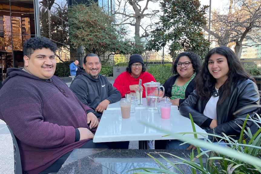 Sherene Magana-Cruz sitting outside at a cafe with her husband and three children smiling.